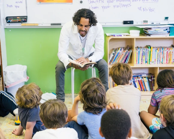 A Teacher in class with kids sitting around him